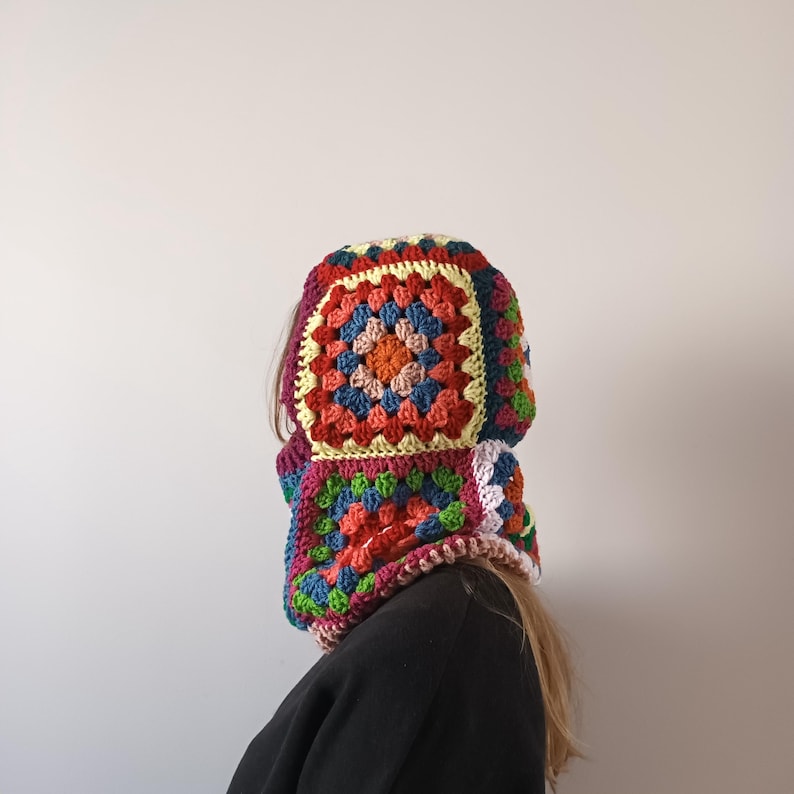 May include: A colourful crocheted hooded neck warmer with a granny square pattern in shades of red, orange, yellow, green, blue, and white.