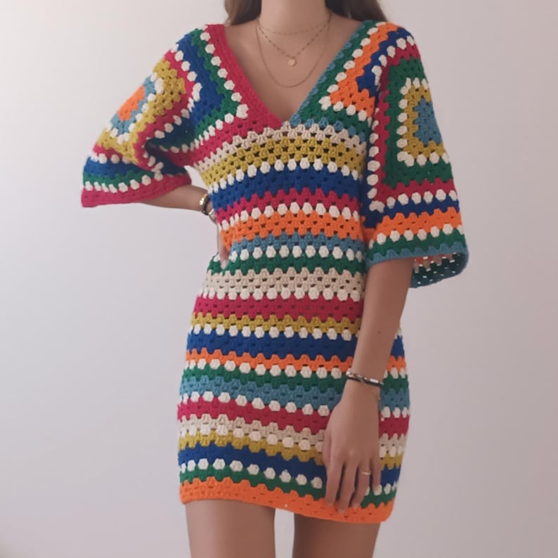 May include: A colorful striped crochet dress with a V-neck and short sleeves. The dress is made with a variety of bright colors, including red, orange, yellow, green, blue, and white.