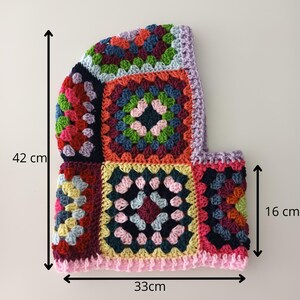 May include: A colourful crocheted hat with a granny square pattern. The hat is 16 cm tall and 33 cm wide. It is made with a variety of colours, including red, green, blue, yellow, and pink.