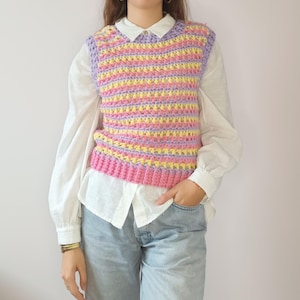 Peut inclure: Un gilet en crochet rayé rose, jaune et violet. Le gilet est sans manches et a un col en V.