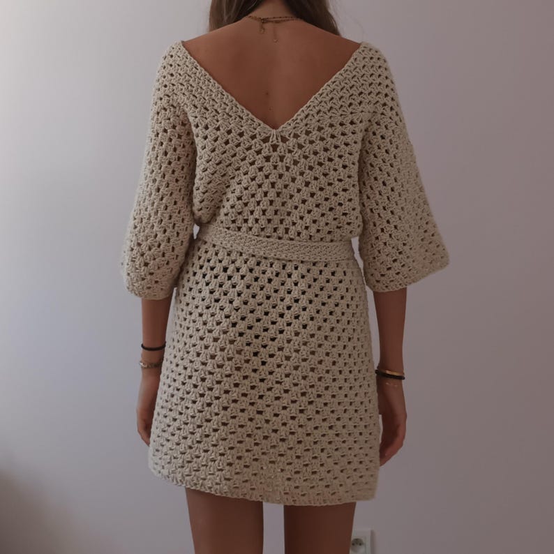 May include: A beige crochet dress with a V-neckline and a belt. The dress has a loose fit and is made of a lightweight, breathable fabric.