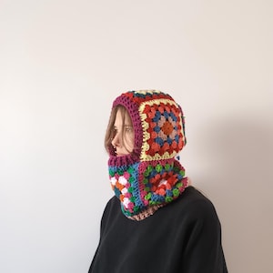 May include: A colourful crocheted balaclava with a geometric pattern. The balaclava is made of different coloured yarn, including red, orange, yellow, green, blue, and purple.