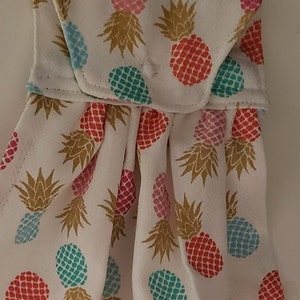 Puede incluir: Toalla de cocina colgante blanca con un colorido estampado de piñas. Las piñas son en tonos rojos, rosas, azules y dorados. La toalla tiene un lazo para colgar y está hecha de tela suave.