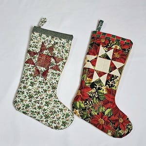 May include: Two Christmas stockings. One is white with a red star design and green holly leaves. The other is red with a white star design and red poinsettias. Both have a green loop for hanging.