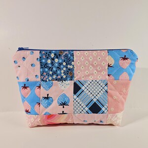 May include: A patchwork zippered pouch with a blue and pink floral pattern. The pouch is made of quilted fabric and has a zipper closure.