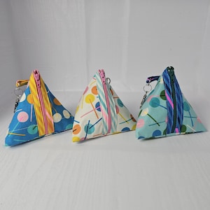 May include: Three triangular zippered pouches with a blue, white, and yellow geometric pattern. The pouches have a zipper closure and a small loop for attaching a key chain.