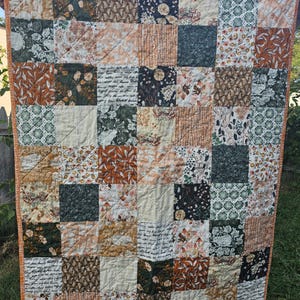 May include: A patchwork quilt with a variety of floral and leaf patterns in shades of brown, green, and cream. The quilt is made up of 25 squares, each with a different design. The quilt is quilted with a diamond pattern.