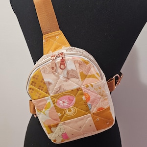 K&ouml;nnte beinhalten: Eine kleine gesteppte Umh&auml;ngetasche mit einem senfgelben Trageriemen und einem Patchwork-Design mit rosa, gelben und wei&szlig;en Blumenmustern.