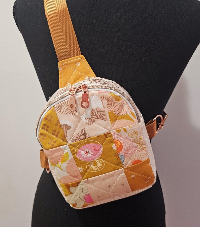 K&ouml;nnte beinhalten: Eine kleine gesteppte Umh&auml;ngetasche mit einem senfgelben Trageriemen und einem Patchwork-Design mit rosa, gelben und wei&szlig;en Blumenmustern.