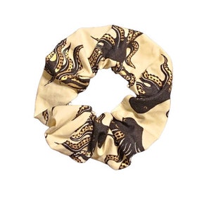 May include: A cream-colored scrunchie with a repeating pattern of black octopus designs. The tentacles have a tan and brown spotted pattern. This hair accessory is a stylish addition to any hairstyle.
