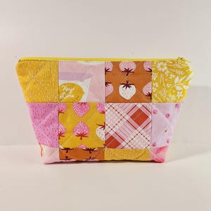 May include: A quilted zippered pouch with a patchwork design featuring pink, yellow, and orange fabric with various patterns including strawberries, lemons, and plaid. The pouch has a yellow zipper.