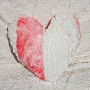 May include: A heart-shaped plush pillow with a pink and white fur design. The pillow is made of soft, fluffy material and is perfect for cuddling.