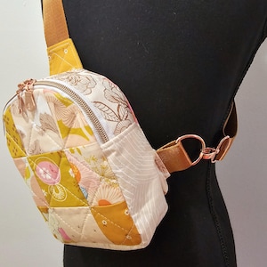 K&ouml;nnte beinhalten: Eine kleine gesteppte Umh&auml;ngetasche mit Blumendruck und einem braunen Riemen. Die Tasche hat einen Rei&szlig;verschluss und eine goldene Metallschnalle.