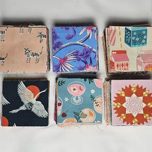 May include: Six stacks of fabric squares with various patterns. Designs include tigers, floral, geometric, and a crane with a rising sun. Colors include pink, blue, teal, and orange. These fabric squares are ideal for quilting and crafting projects.