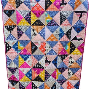 May include: A colorful patchwork quilt with a vibrant mix of patterns and colors. The quilt features a variety of fabrics in triangles, including pink, blue, yellow, and black, with a pink border. The quilt is held up by two hands.