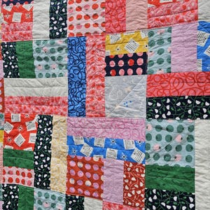May include: A patchwork quilt with a variety of colorful fabrics, including red, pink, blue, green, yellow, and white. The quilt is made up of squares and rectangles, and the fabrics are sewn together in a random pattern. The quilt is made of cotton fabric and has a soft, comfortable feel.