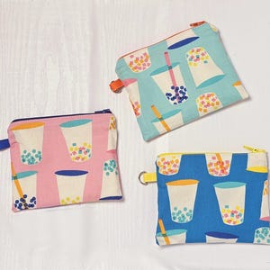 May include: Three small, zippered pouches with a repeating pattern of bubble tea cups. One pouch is pink, one is blue, and one is teal. Each pouch has a different colored zipper and a small loop for attaching a key ring.