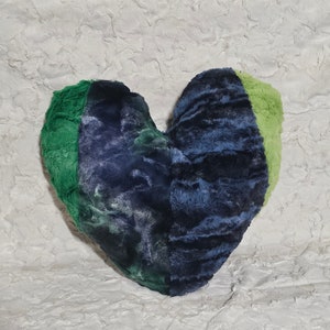 May include: A heart-shaped plush pillow with a patchwork design. The pillow is made of three different colors of faux fur: green, blue, and light green.