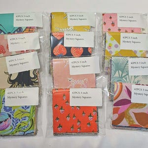 May include: A collection of 10 packages of 3-inch fabric squares, each with a unique patterned design. The fabrics feature various colors and motifs, including strawberries, floral patterns, and abstract designs. Each package contains 42 pieces and includes a label.