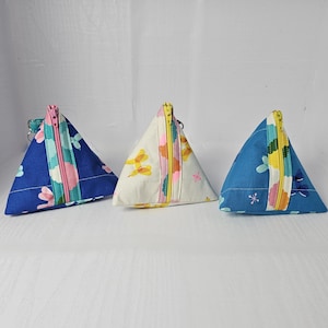 May include: Three triangular zippered pouches with different floral patterns. The pouches are made of fabric and have a zipper closure. The pouches are blue, white, and blue with pink accents.