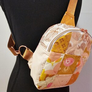 K&ouml;nnte beinhalten: Eine kleine, gesteppte Umh&auml;ngetasche mit Patchwork-Design in Rosa-, Gelb- und Wei&szlig;t&ouml;nen. Die Tasche hat einen Rei&szlig;verschluss und einen ros&eacute;goldenen Riemen.