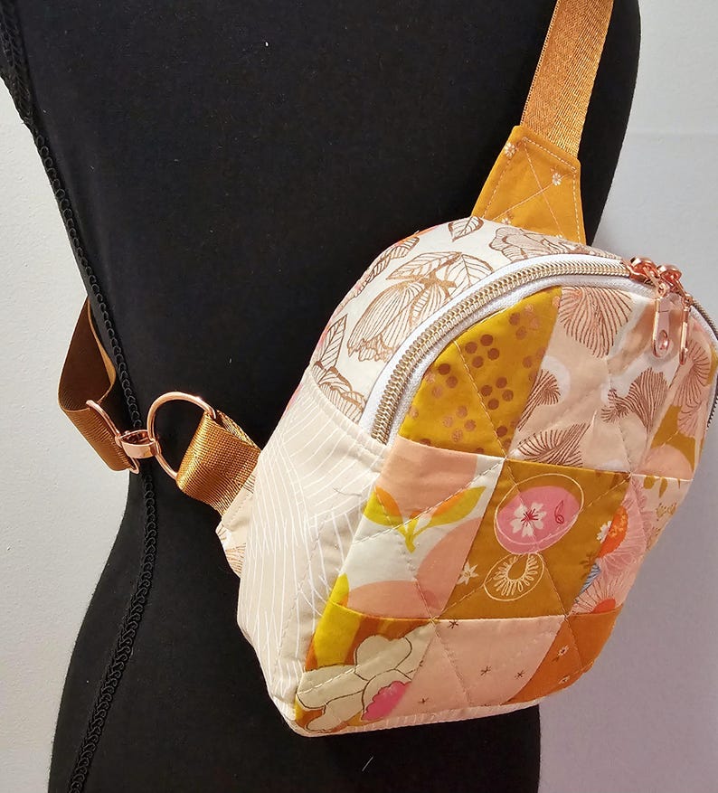 K&ouml;nnte beinhalten: Eine kleine, gesteppte Umh&auml;ngetasche mit Patchwork-Design in Rosa-, Gelb- und Wei&szlig;t&ouml;nen. Die Tasche hat einen Rei&szlig;verschluss und einen ros&eacute;goldenen Riemen.