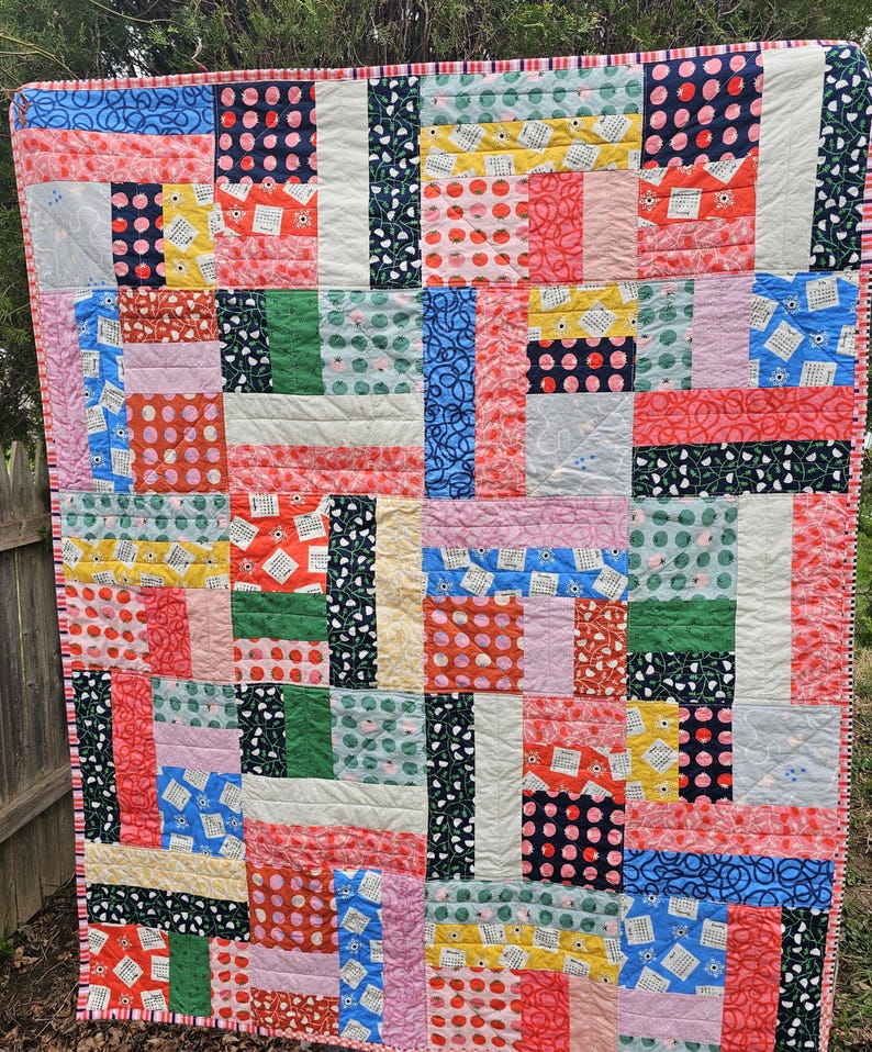 May include: A colorful patchwork quilt with a variety of patterns, including polka dots, floral designs, and geometric shapes. The quilt is made up of squares and rectangles in shades of pink, red, yellow, green, blue, and white.