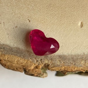 May include: A heart-shaped, faceted ruby gemstone with a deep red colour.