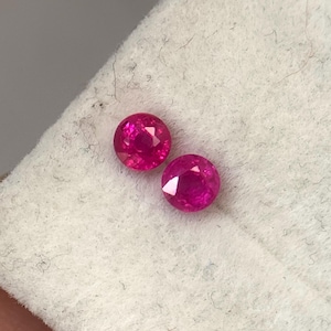 以下が含まれることがあります： 白い表面に置かれた、2つの丸い鮮やかなピンクの宝石