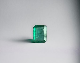 May include: A vibrant green emerald gemstone with a rectangular cut and a polished finish.