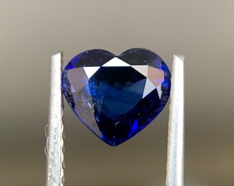 May include: A deep blue heart-shaped sapphire gemstone held in tweezers.