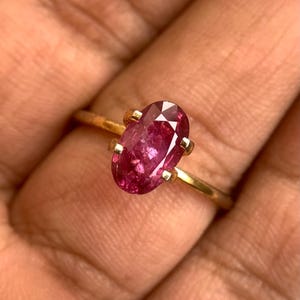 Peut inclure: Une bague en or avec une pierre ovale rose. La bague est sur un doigt.
