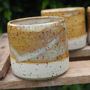 Könnte beinhalten: Zwei Keramikbecher mit einem gesprenkelten braunen und weißen Überzug. Die Becher stehen auf einem Holzregal.