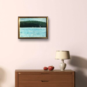 May include: A framed painting of a seascape with sailboats in the water. The water is a light blue color and the sky is a light blue color. The sailboats are white and there are trees in the background.