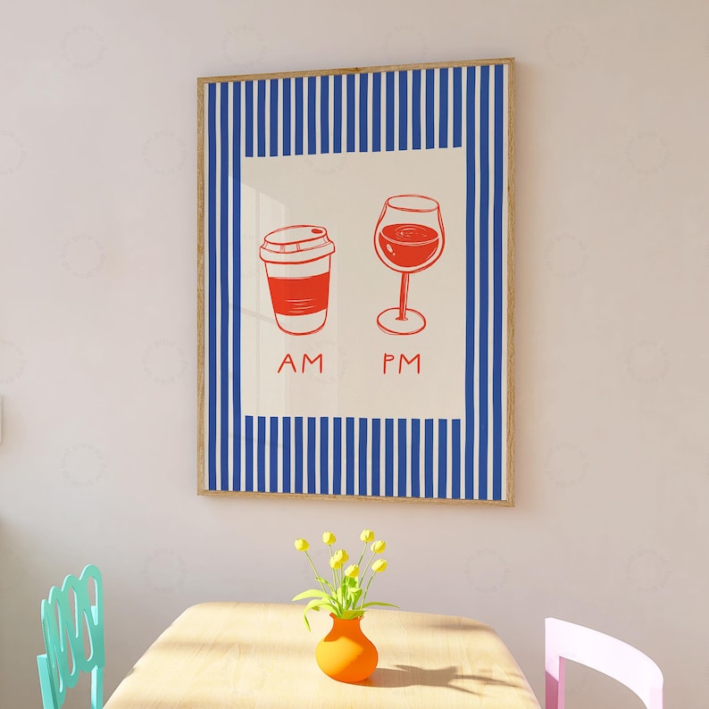 May include: A framed art print featuring a red coffee cup labeled "AM" and a red wine glass labeled "PM". The artwork is set against a cream background with a blue and white striped border. The print is in a wooden frame.