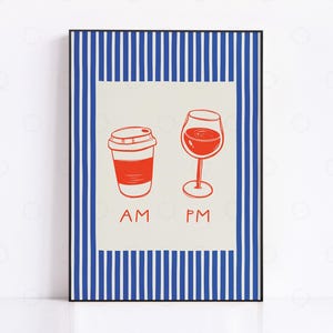 May include: A framed art print featuring a red coffee cup and a wine glass, with the text "AM" and "PM" below. The artwork has a cream-colored background with a blue and white striped border. The print is in a black frame.