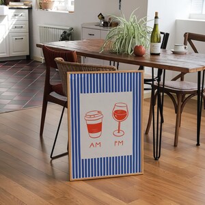 May include: A framed print featuring a red coffee cup and wine glass, with "AM" and "PM" text. The print has a white background with blue vertical stripes and a wooden frame. The image is set in a dining room.