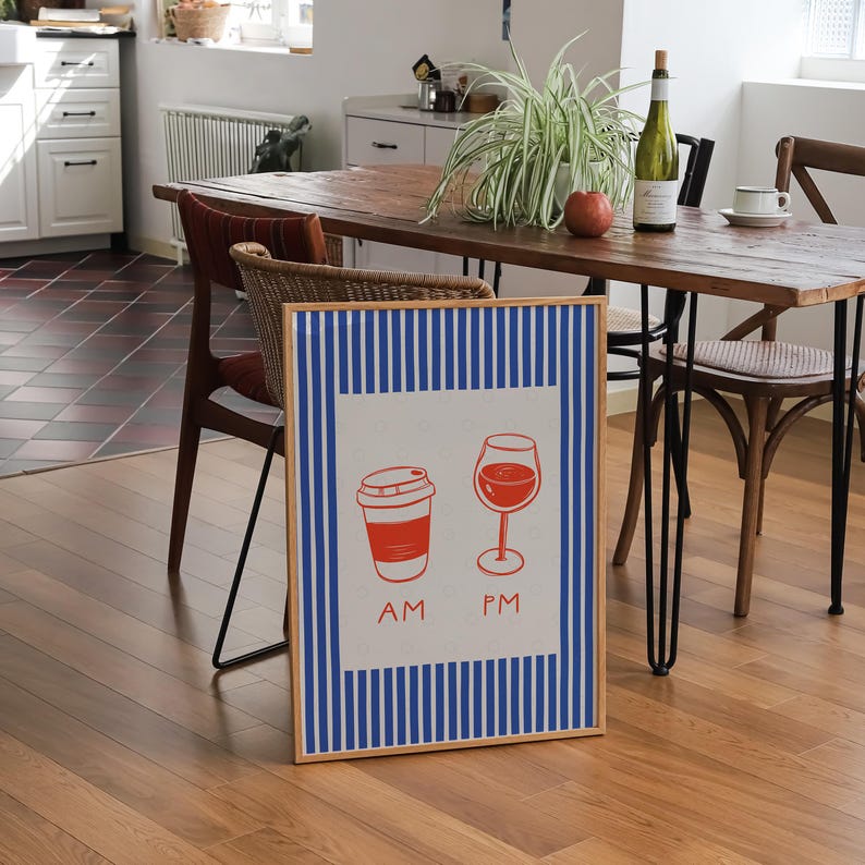 May include: A framed print featuring a red coffee cup and wine glass, with "AM" and "PM" text. The print has a white background with blue vertical stripes and a wooden frame. The image is set in a dining room.