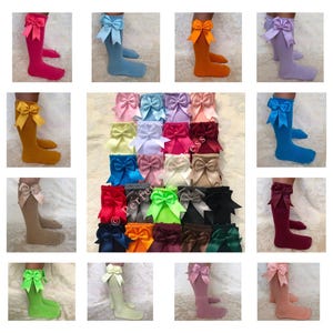 K&ouml;nnte beinhalten: Eine Sammlung von kniehohen Socken mit verschiedenen farbigen Schleifen. Die Socken sind alle wei&szlig; und die Schleifen sind in Farben wie Rot, Blau, Gr&uuml;n, Gelb, Rosa und Lila.