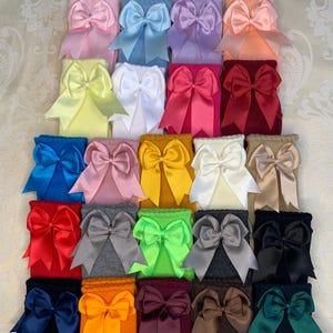 K&ouml;nnte beinhalten: Eine Sammlung von 24 kniehohen Socken mit gro&szlig;en Satinb&auml;ndern in verschiedenen Farben, darunter rosa, blau, gelb, rot, gr&uuml;n und braun.