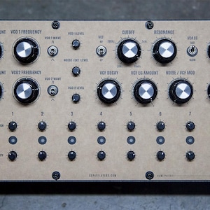May include: A beige and brown synthesizer with knobs and buttons. The synthesizer has a wooden frame and a metal faceplate. The faceplate has the text "VCG Decay", "VCG 1 FM Amount", "VCG 1 Frequency", "Cutoff", "Resonance", "Volume", "1-2 FM Amount", "VCG 2 FM Amount", "VCG 2 Frequency", "VCG Decay", "VCG FM Amount", "VCG VCG", "Tempo", and "Modular System" printed on it.