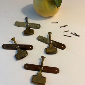 May include: Four antique brass and metal clamps with screws, and a yellow pear with a green leaf. The clamps have a rectangular base and a pivoting head. Small nails are scattered nearby. The pear is a light yellow color.