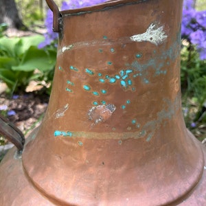 May include: A large copper pitcher with a handle. The pitcher has a patina of green and white spots.