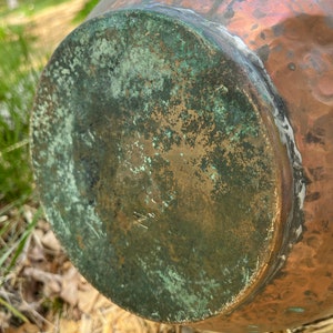 May include: A copper pot with a green patina on the bottom. The pot has a hammered texture and a rounded shape.