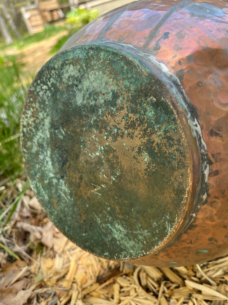 May include: A copper pot with a green patina on the bottom. The pot has a hammered texture and a rounded shape.