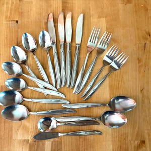 May include: A collection of stainless steel flatware including four dinner knives, four dinner forks, and eight spoons of varying sizes. Each piece features a polished silver finish and a subtle etched floral pattern on the handle.