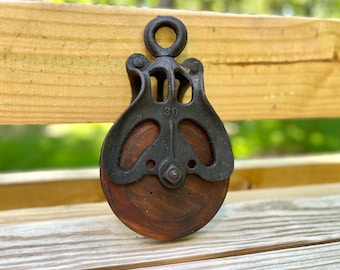 May include: A vintage wooden pulley with a black metal frame and a number "30" printed on the side. The pulley is mounted on a wooden surface.