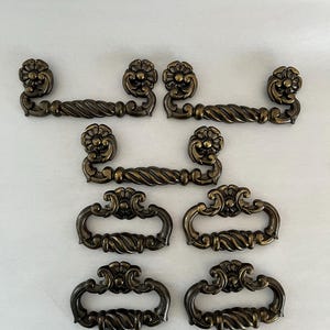 May include: Set of eight antique brass cabinet pulls with ornate floral designs. The pulls have a twisted rope design and come in two sizes.