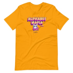 May include: Yellow short-sleeved t-shirt with a cartoon cat wearing a pink donut and the text "Alphabet Mafia" in a colorful, stylized font.