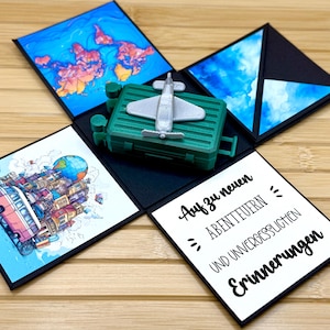 Könnte beinhalten: Eine schwarze Explosionsbox mit einem grünen Koffer, einem Spielzeugflugzeug und einer Weltkarte auf der Oberseite. Die Box hat einen weißen Hintergrund mit dem Text "Auf zu neuen Abenteuern und unvergesslichen Erinnerungen".